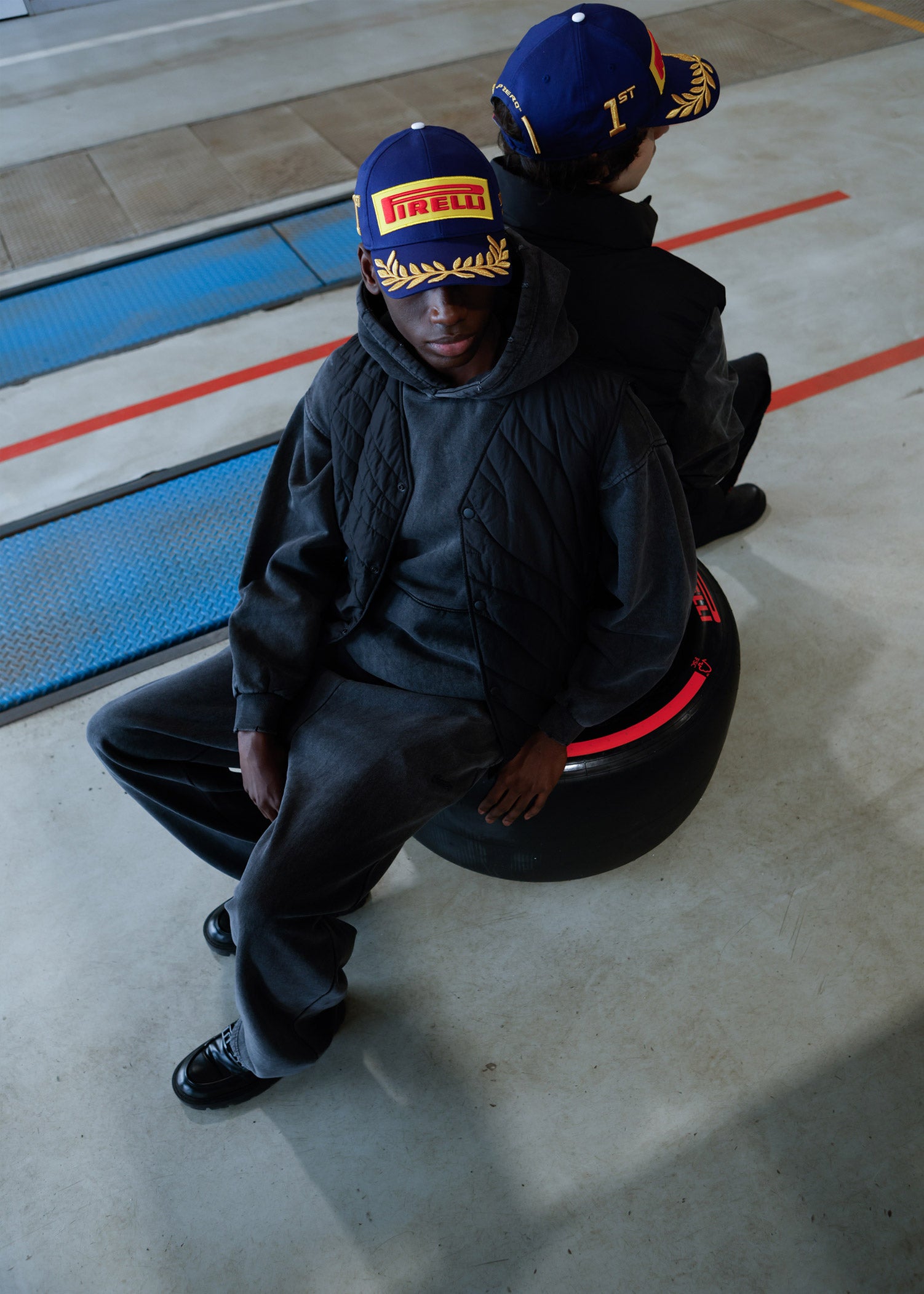 two men in blue Pirelli Podium Caps sitting on Pirelli tyre
