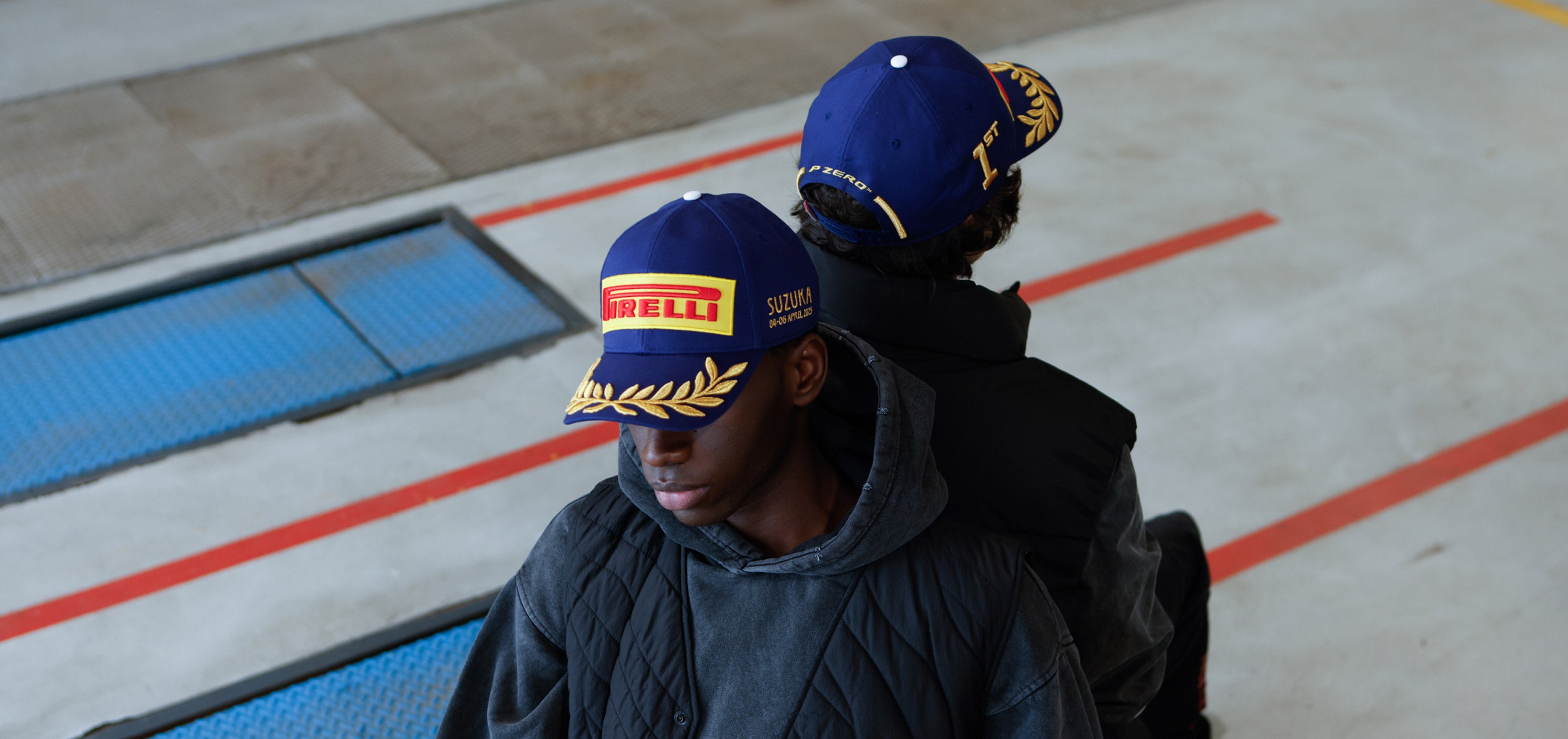 two men in blue Pirelli Podium Cap in race garage